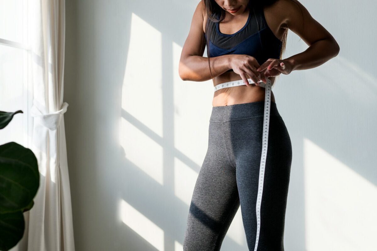 Patient measuring waist after laser lipo recovery to track body contouring results and healing progress.