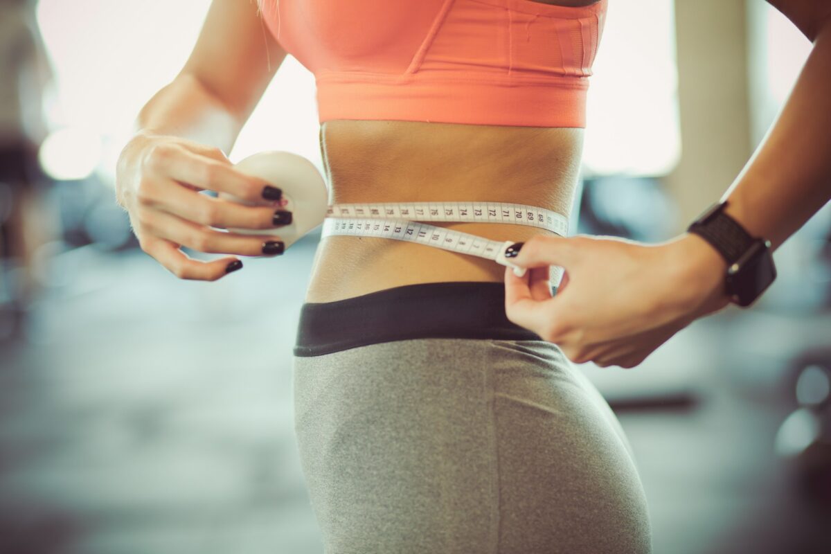 Woman measuring her waist after a tummy tuck while evaluating body contouring results during recovery.