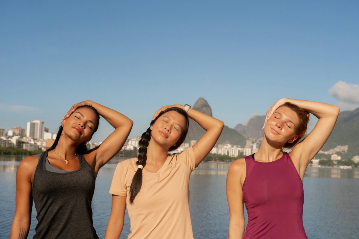 Three women stretching outdoors after recovery from capsular contracture treatment or breast explant surgery.