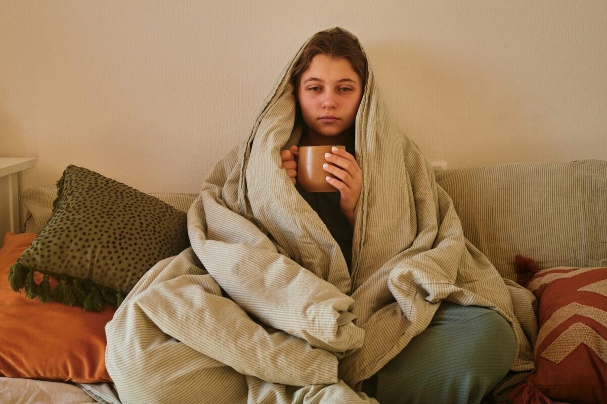 Woman wrapped in a blanket holding a warm drink during recovery after surgery in cold weather.