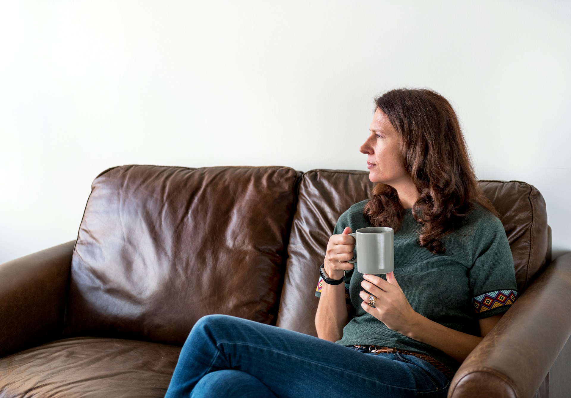 Woman sitting thoughtfully on a couch while considering whether to meet with a breast lift surgeon about breast lift or reduction options.