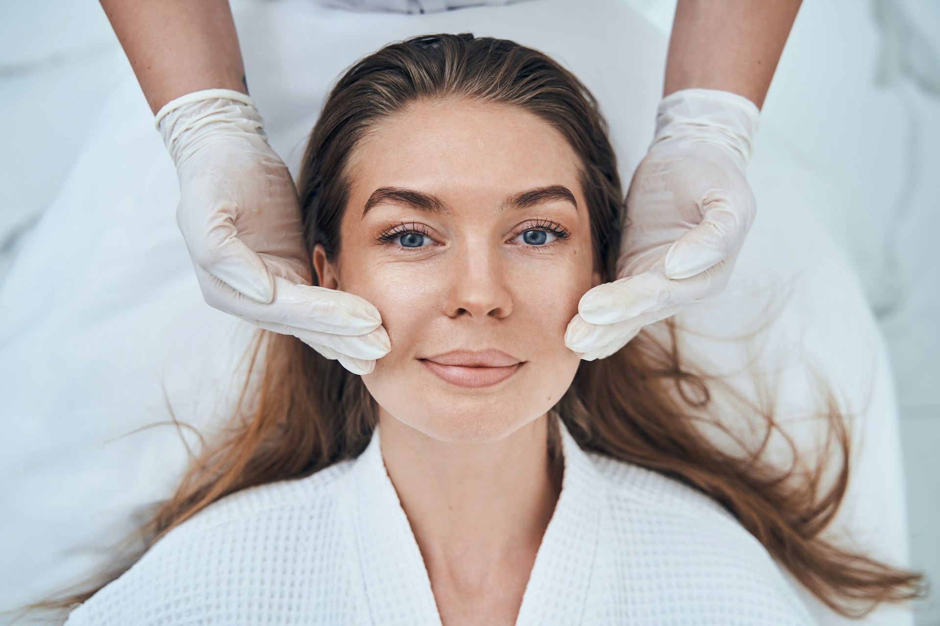Woman receiving a facial rejuvenation treatment from a skincare professional in a bright treatment room.