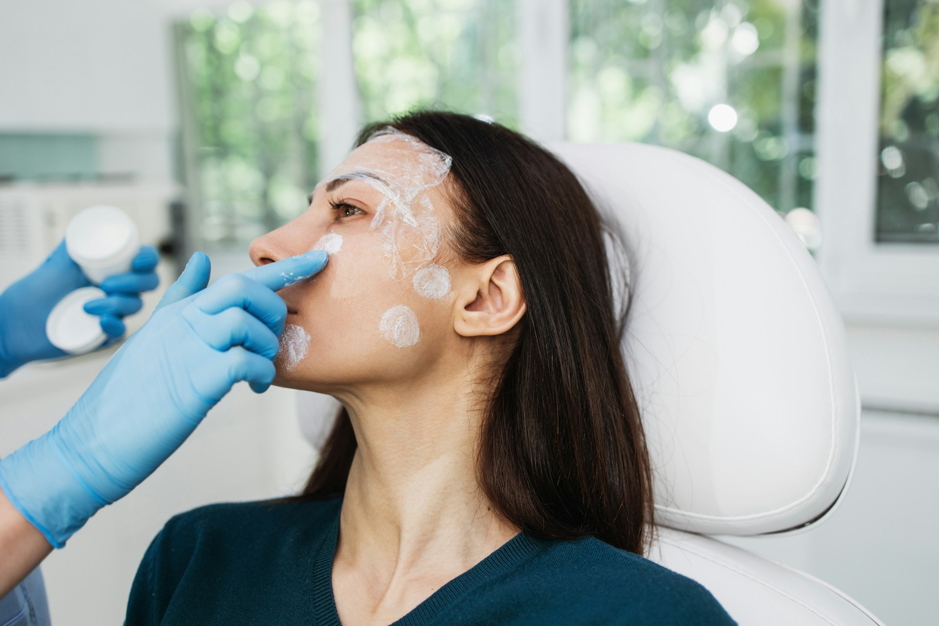 Woman receiving facial preparation in a clinical setting while exploring cosmetic surgery and aesthetic treatment options.