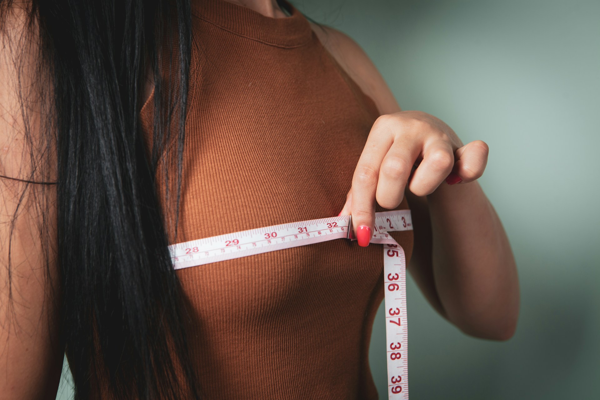 Woman measuring her chest while considering breast augmentation surgery and personalized implant sizing options.