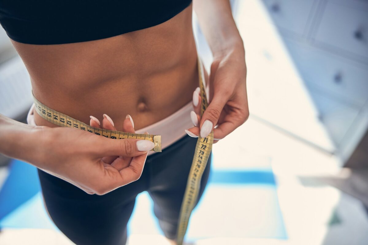 Woman measuring her waist while planning body contouring before the holiday season.